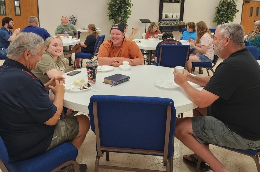 People sharing food and conversation around a table at Faith Baptist Church.